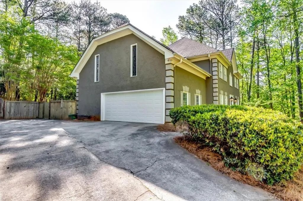 View of property exterior featuring stucco siding, a shingled roof, a garage, driveway, and a gate