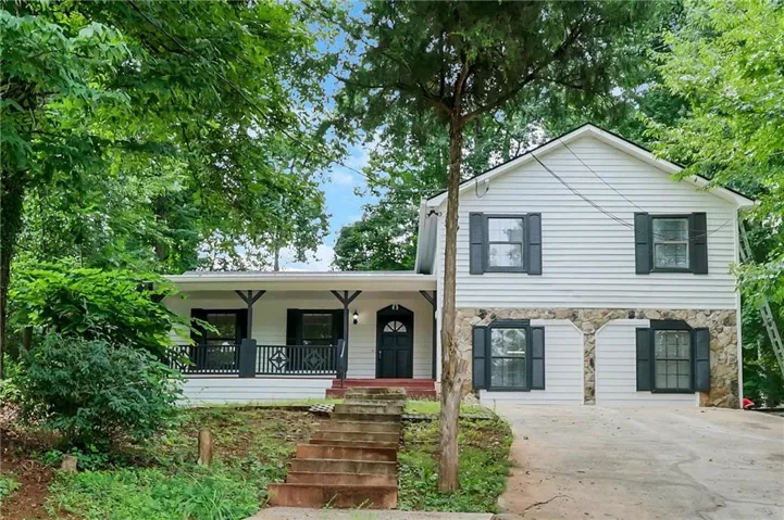 White siding exterior with a stone facade, arched entryway, covered porch, and dark window shutters