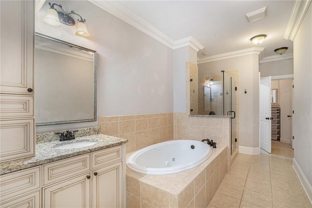 Bathroom featuring tile flooring, crown molding, large vanity, and shower with separate bathtub