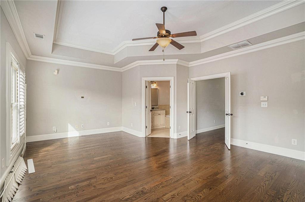 Empty room with dark hardwood / wood-style floors, a raised ceiling, crown molding, and ceiling fan