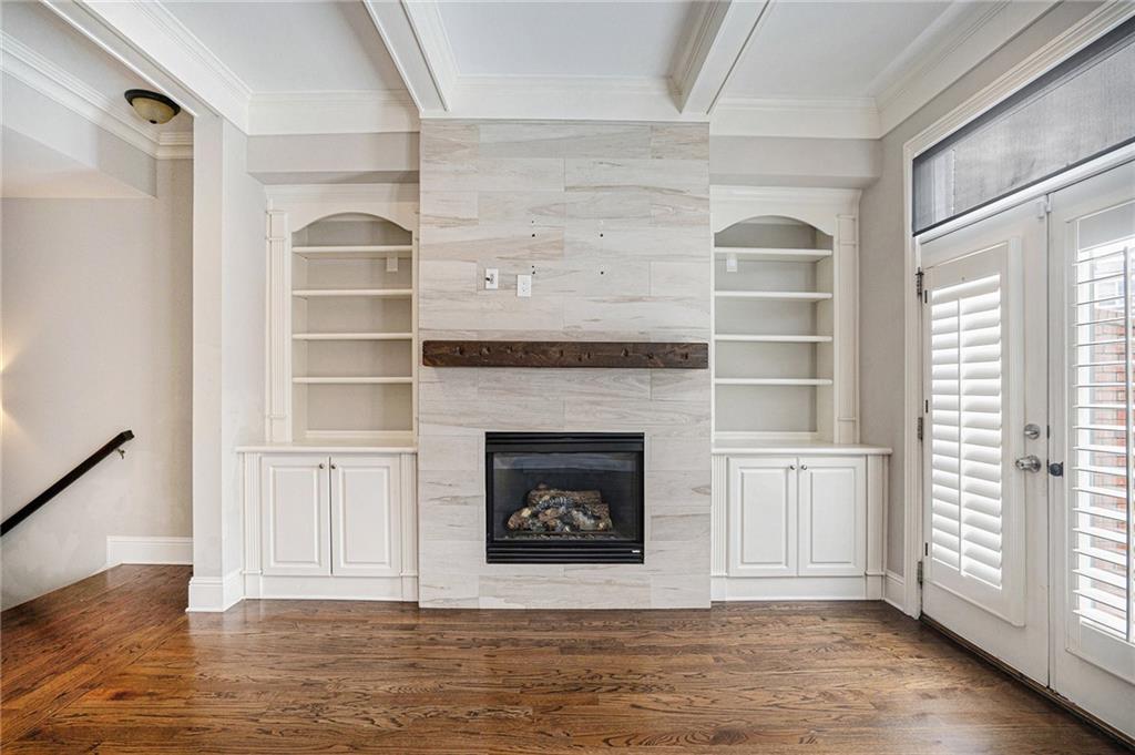 Unfurnished living room featuring crown molding, a tiled fireplace, built in shelves, and dark wood-type flooring
