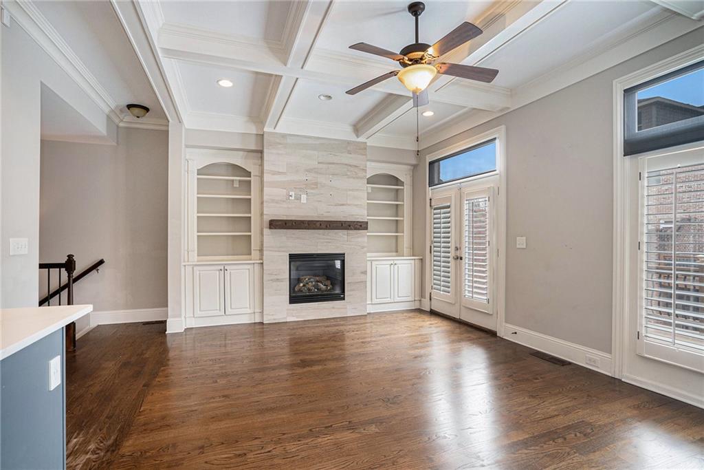 Unfurnished living room with dark hardwood / wood-style floors, built in shelves, coffered ceiling, and a fireplace