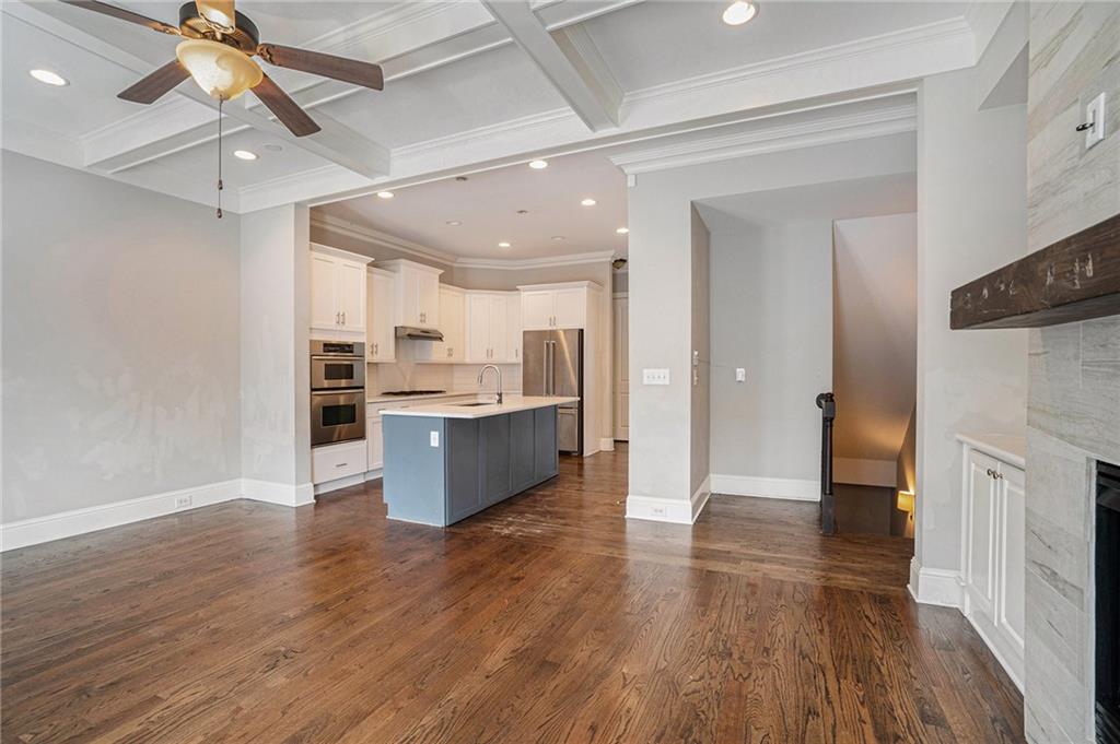 Kitchen with a large fireplace, ceiling fan, white cabinetry, dark hardwood / wood-style floors, and an island with sink