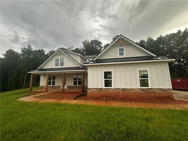 New construction residence featuring a covered front porch with natural wood columns, a stone foundation, board and batten siding, and a black metal roof