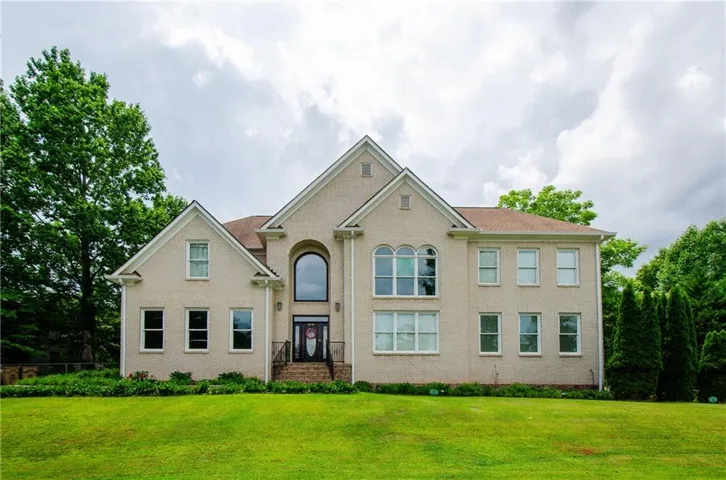 Traditional two-story residence featuring a light-colored brick facade and a prominent arched window at the entry