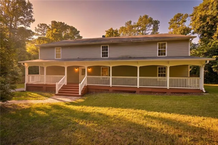 Expansive wrap-around porch with white railings, a large front lawn, and surrounding mature trees