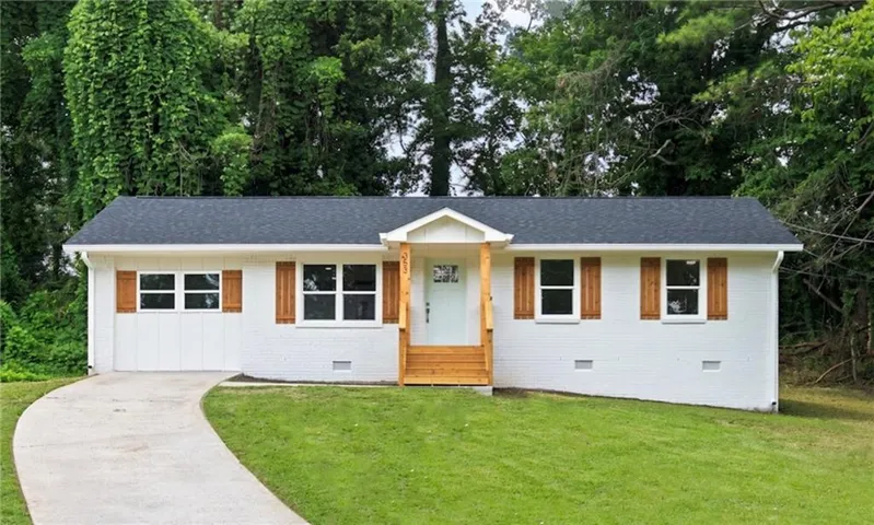 White exterior with wood-tone shutters, dark shingle roof, light blue front door, and wooden porch with stairs