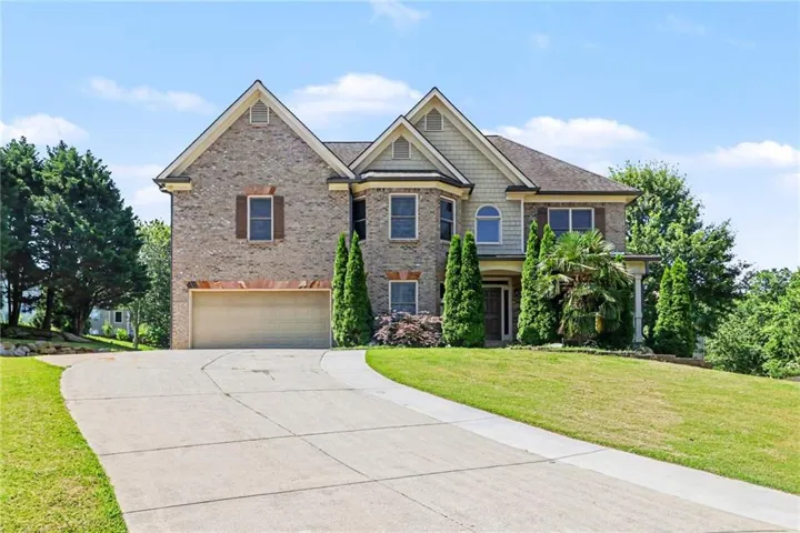 Brick and siding exterior featuring a two-car garage, bay windows, gabled rooflines, and mature landscaping