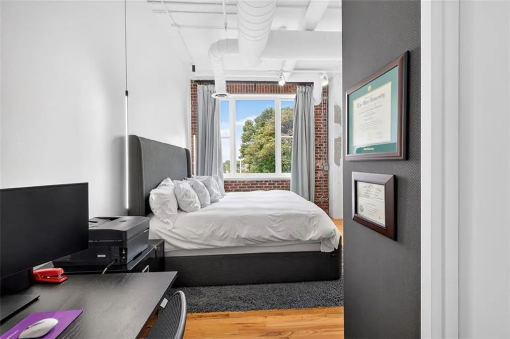 Hardwood flooring, exposed brick wall, large window with natural light, exposed ceiling ductwork, and track lighting