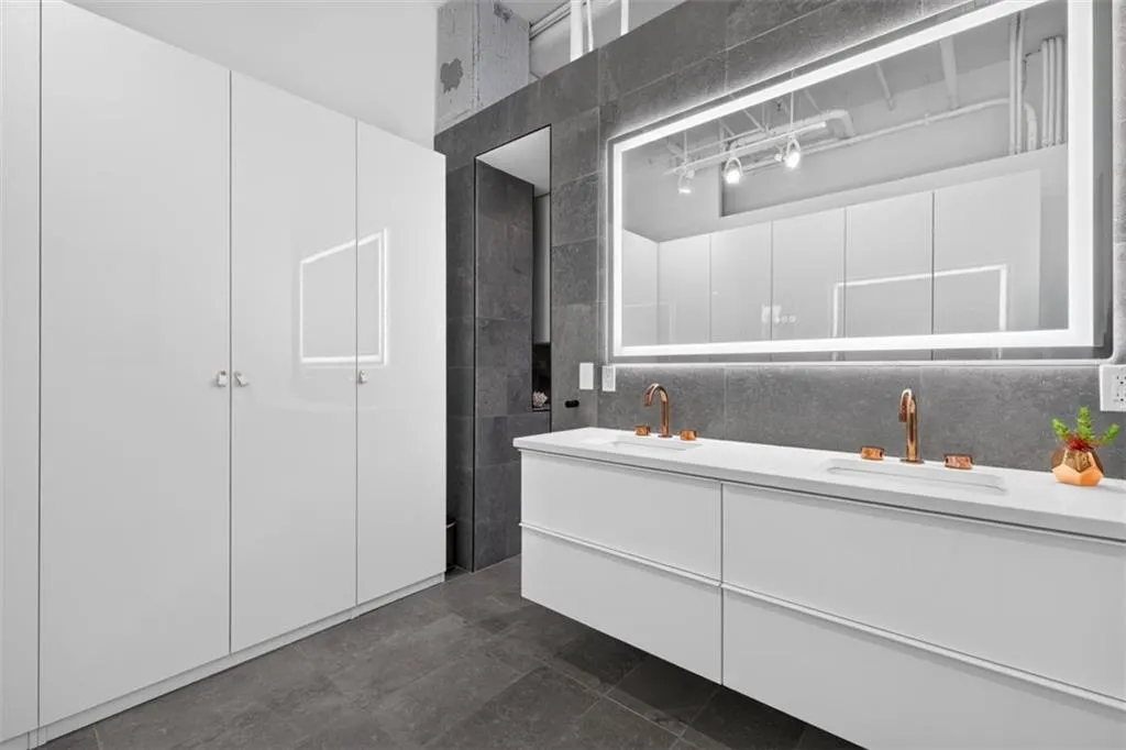 Modern primary bathroom featuring a floating double-sink vanity with white cabinetry and integrated storage, quartz countertop, and dual brass fixtures