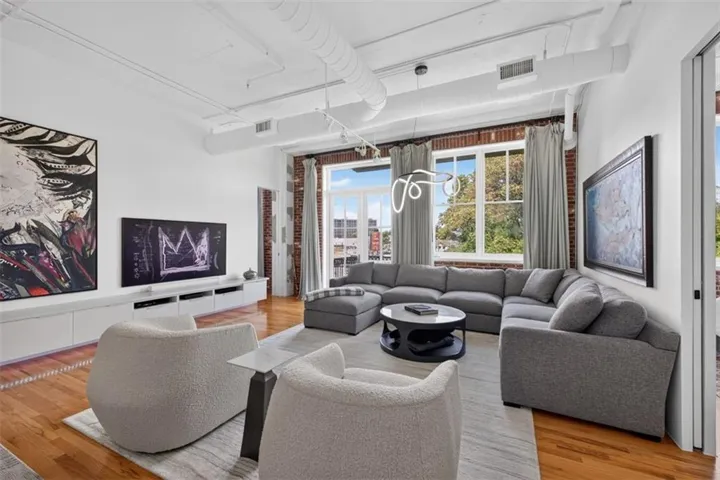 Exposed brick wall, hardwood flooring, high ceilings with exposed ductwork, large multi-pane windows, and built-in wall cabinetry