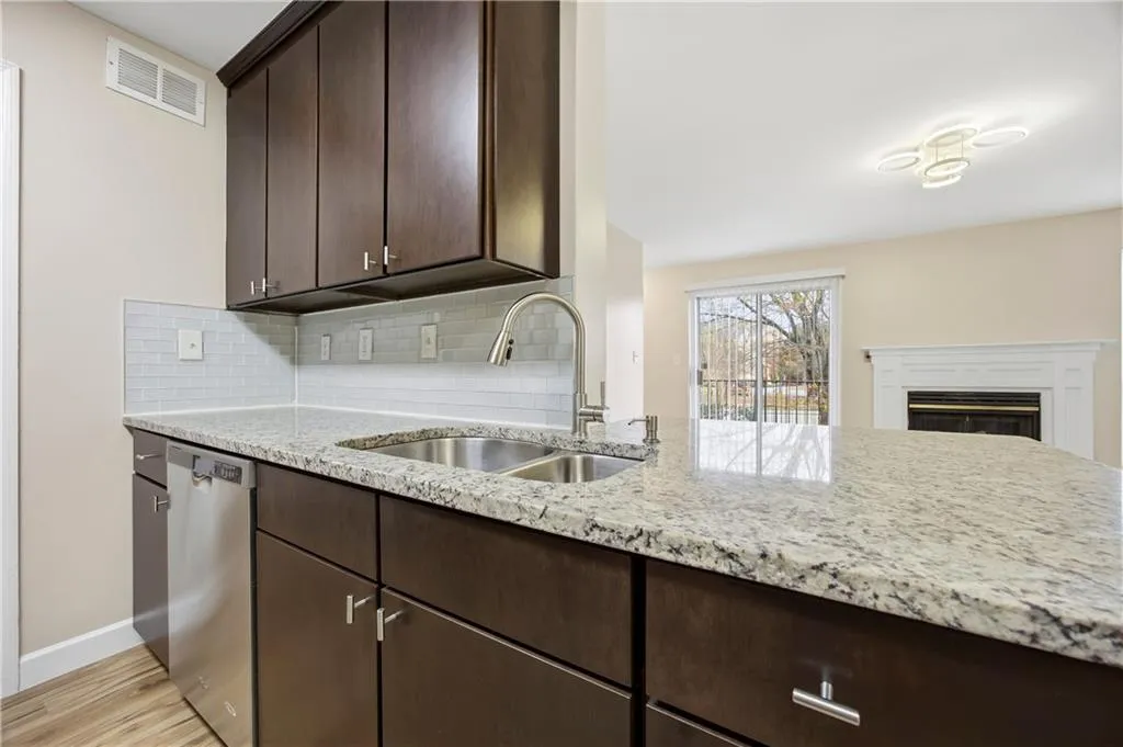 Kitchen featuring dark wood finish cabinets, light stone counters, and dishwasher