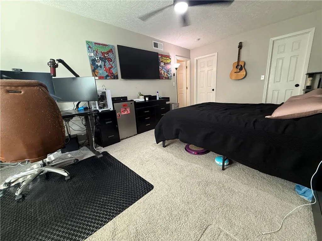 Carpeted bedroom featuring a textured ceiling, an office area, and a ceiling fan