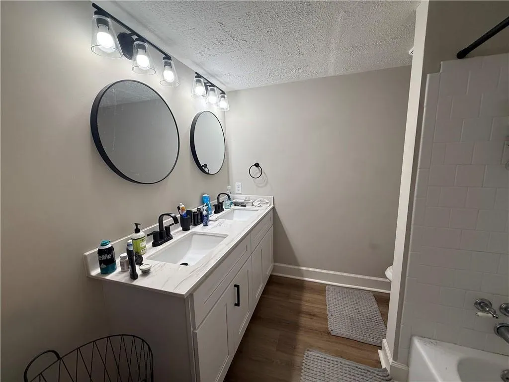 Full bathroom with a textured ceiling, double vanity, dark wood-style flooring, and bathing tub / shower combination
