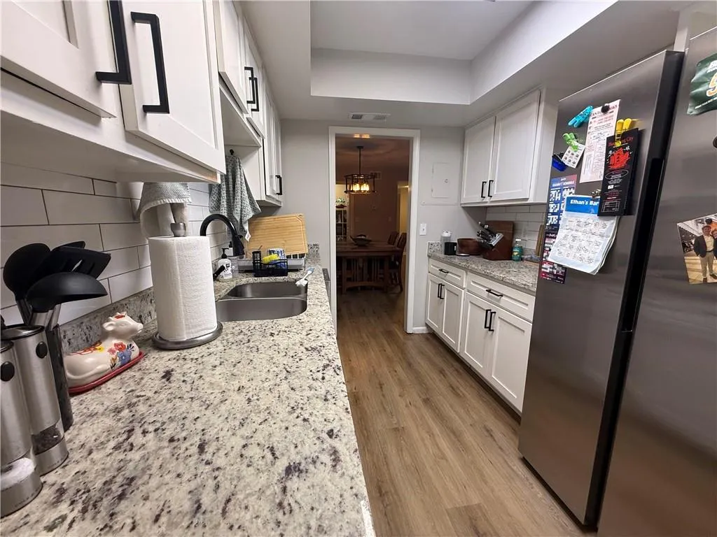 Kitchen featuring freestanding refrigerator, decorative backsplash, white cabinetry, light wood-type flooring, and light stone counters