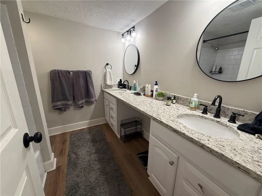 Full bathroom featuring a textured ceiling, double vanity, dark wood-style floors, and a shower