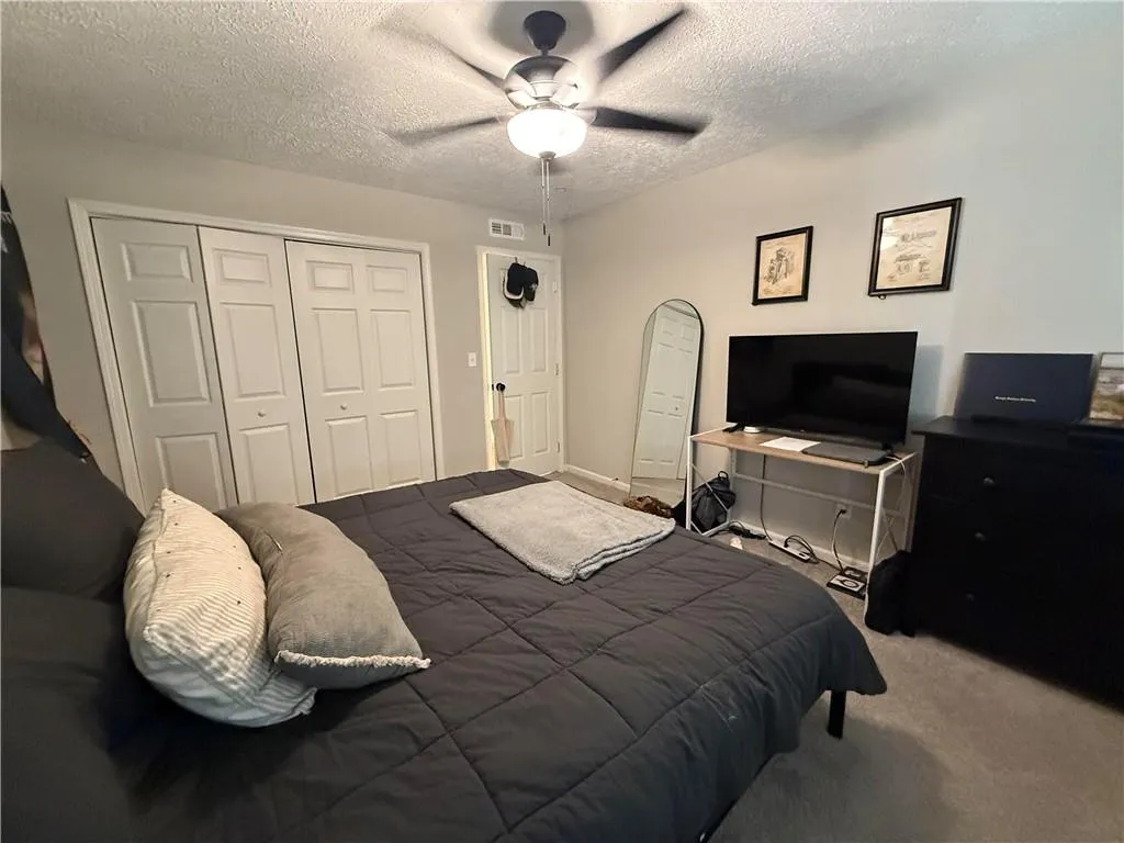 Bedroom with a textured ceiling, carpet floors, a closet, and a ceiling fan