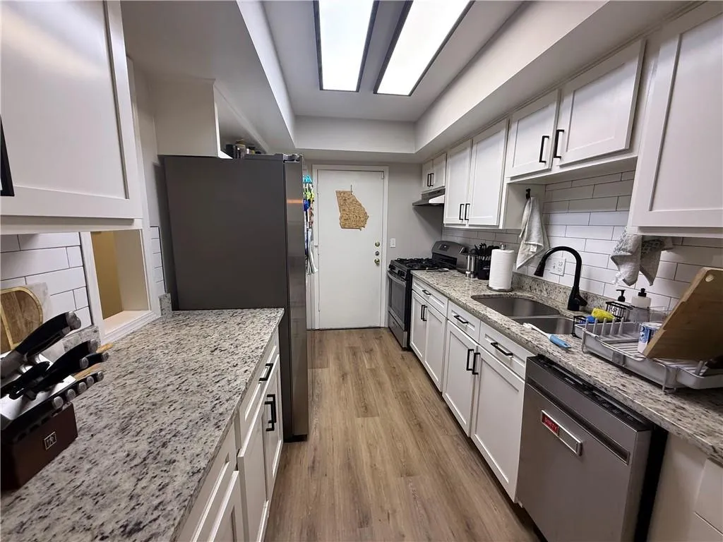 Kitchen featuring decorative backsplash, white cabinetry, stainless steel appliances, and light stone counters