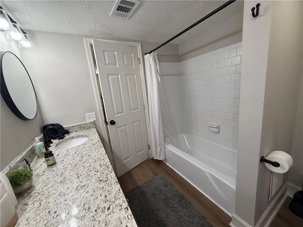 Full bathroom featuring shower / tub combo with curtain, a textured ceiling, dark wood-style flooring, and vanity