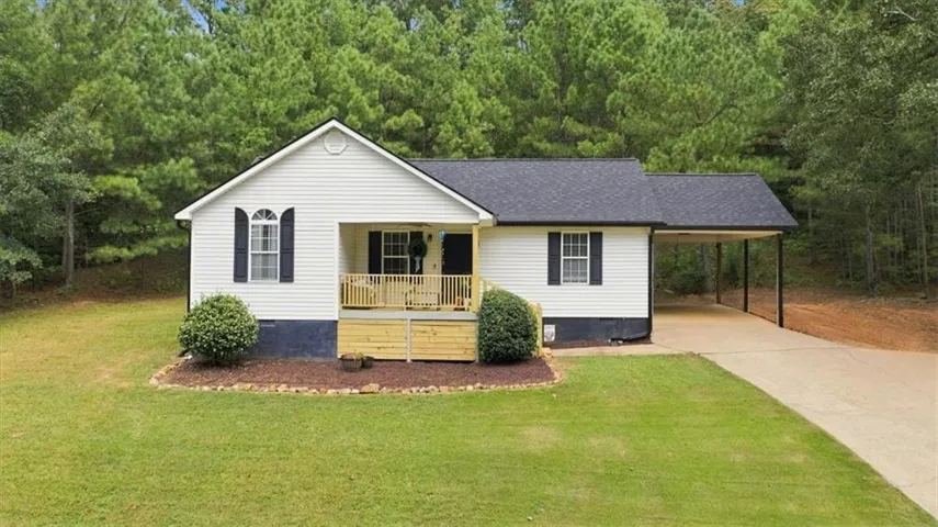 White siding exterior with a dark shingle roof, a covered porch with natural wood railing, a concrete driveway, and an attached carport
