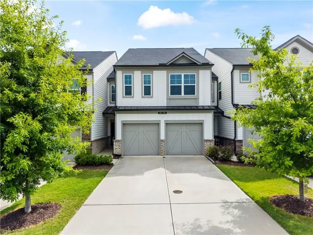 Two-story townhome with a dark gray roof, white siding, and stone accents