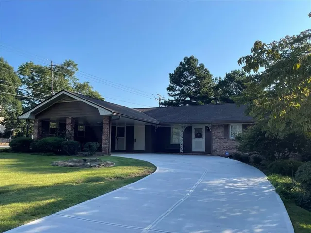 Brick facade residence featuring a covered front porch with brick columns, a newly paved concrete driveway, a gabled roofline, and established landscaping