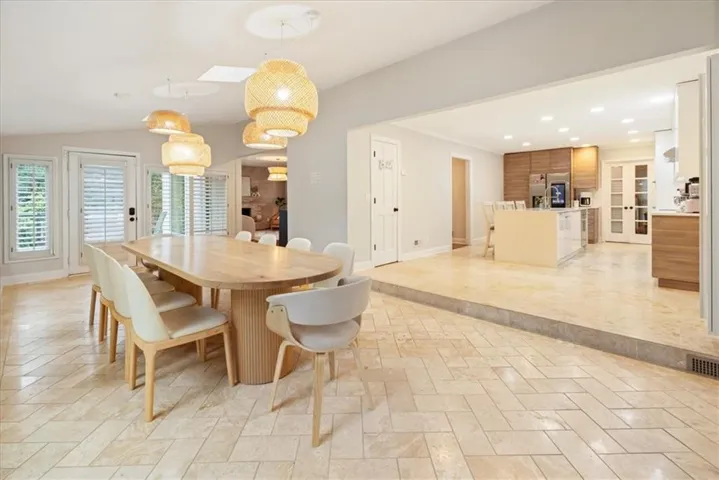 Expansive dining area featuring a light wood-finish table with a fluted pedestal base, herringbone-patterned tile flooring, and multiple woven pendant light fixtures