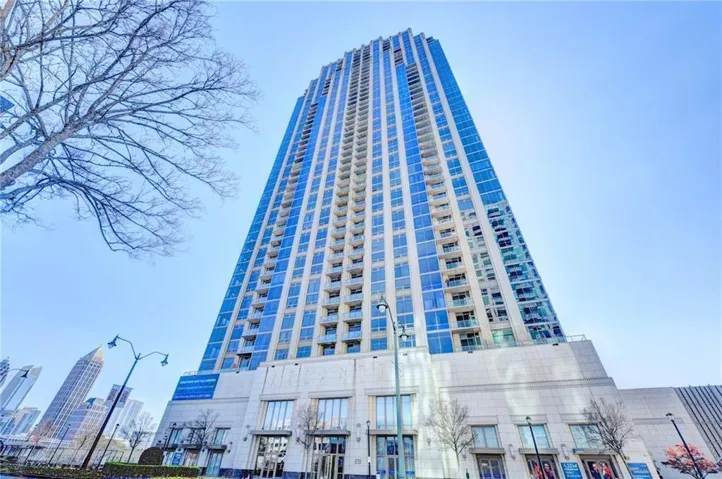 Contemporary high-rise building featuring extensive glass curtain walls, multiple private balconies, and a stone-clad base with large storefront windows