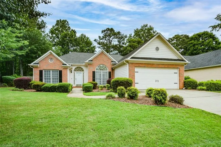 Brick exterior with white trim, arched transom window over the entry, attached two-car garage, and established front landscaping