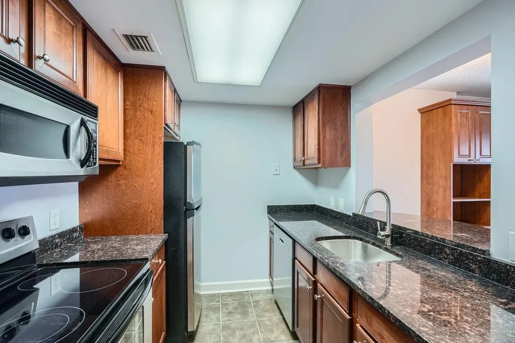 Kitchen with stainless steel appliances, a sink, dark stone countertops, baseboards, and light tile patterned floors
