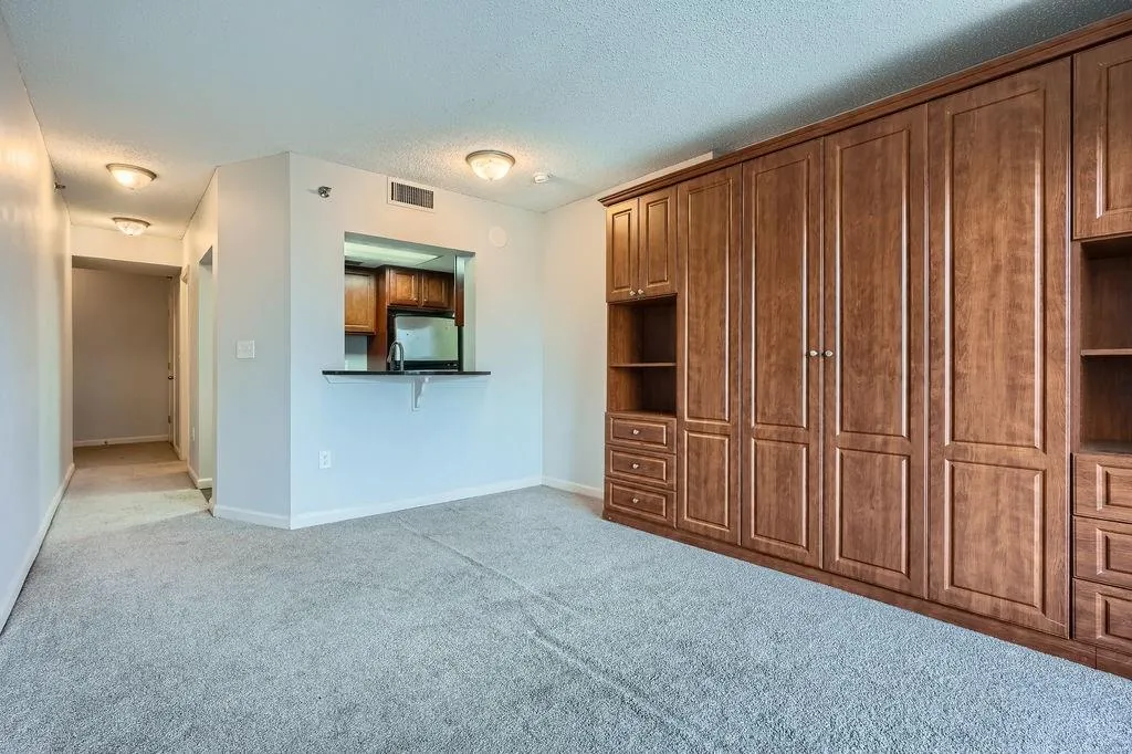 Unfurnished living room with light colored carpet, a textured ceiling, and baseboards