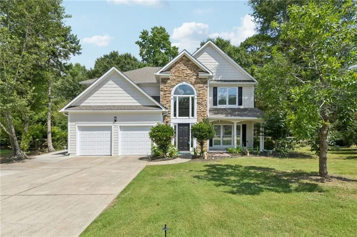 Two-story residence featuring a stone and siding exterior, arched window over the main entry, a two-car garage, and a concrete driveway