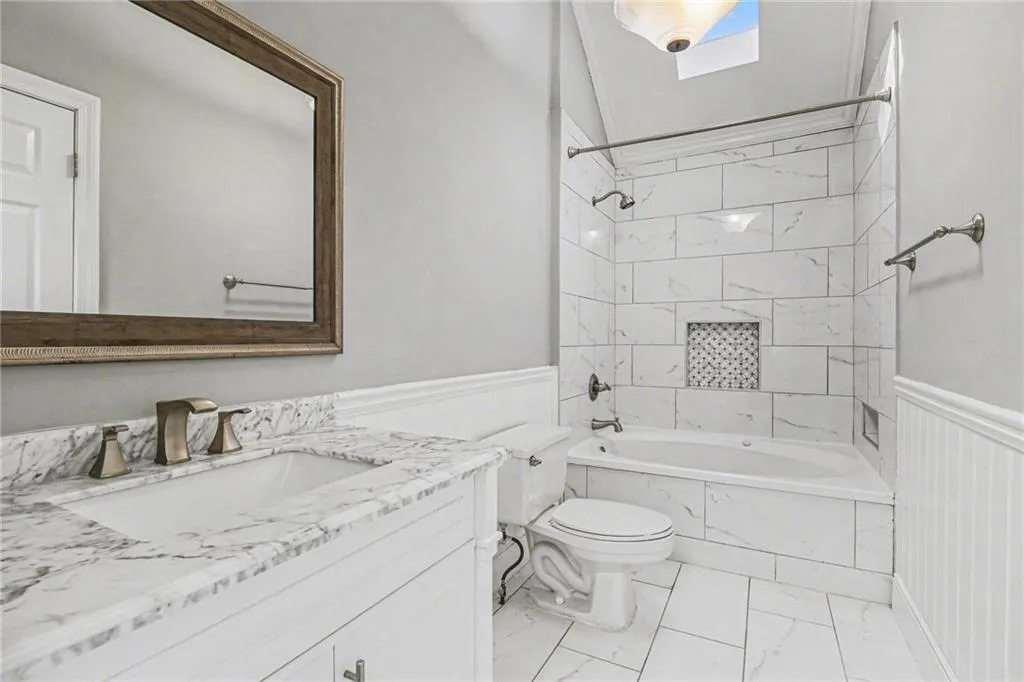 Full bath with shower / bath combination, vanity, wainscoting, and light marble finish floors