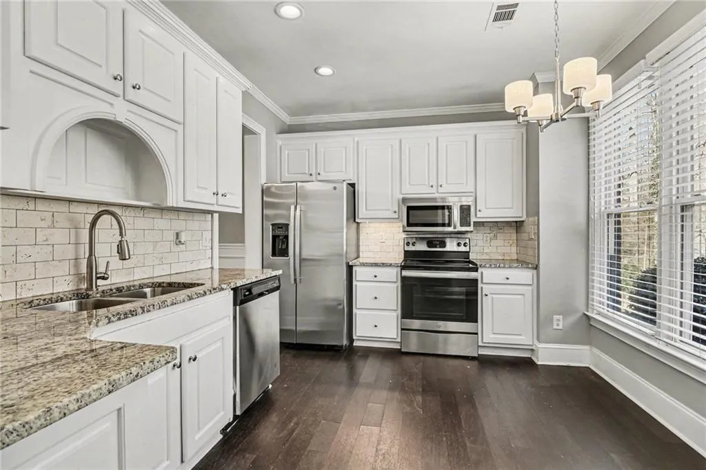Kitchen featuring light stone countertops, white cabinets, stainless steel appliances, dark wood-style flooring, and ornamental molding