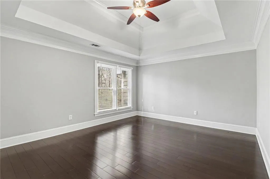 Unfurnished room with a ceiling fan, ornamental molding, a tray ceiling, and dark wood-type flooring