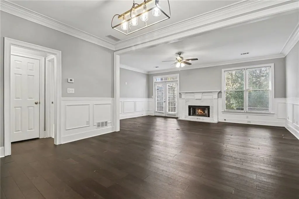 Unfurnished living room featuring a wainscoted wall, a premium fireplace, dark wood-style floors, a decorative wall, and ornamental molding
