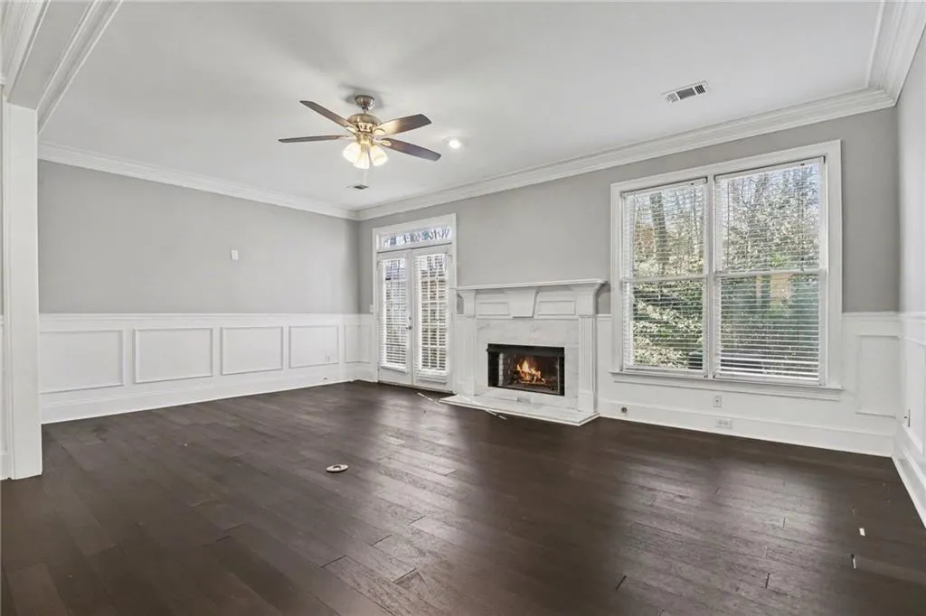 Unfurnished living room with a decorative wall, wainscoting, crown molding, ceiling fan, and a fireplace