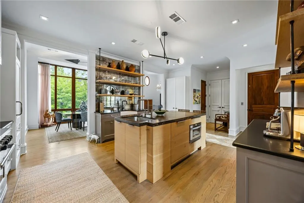Kitchen featuring wood-finish flooring, a central island with integrated oven, custom cabinetry, a contemporary chandelier, and open shelving with an antique mirror backsplash