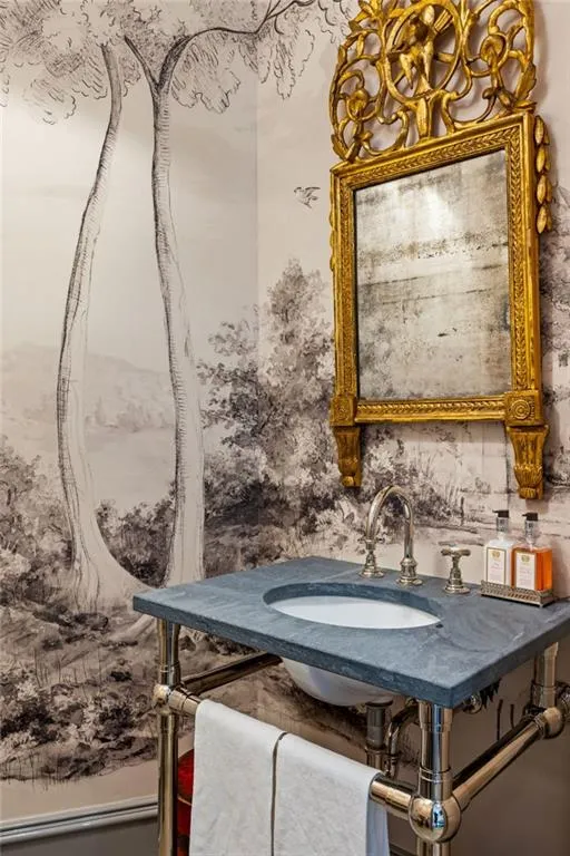 Pedestal sink with a stone countertop, chrome fixtures, and a decorative gold-framed mirror