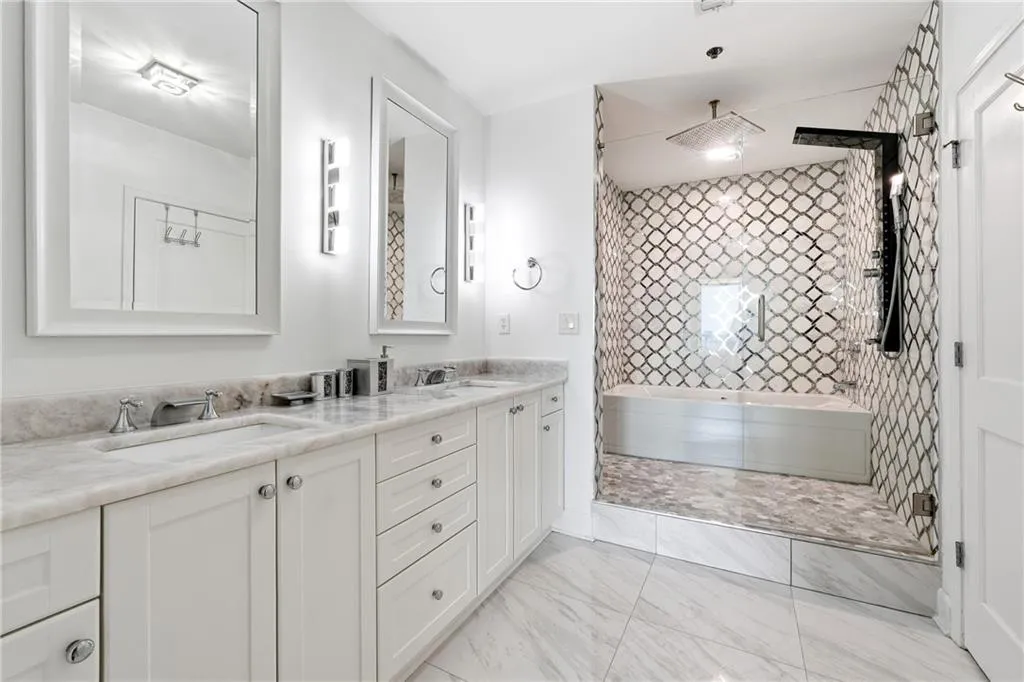 Full bath featuring double vanity, tiled shower, and light marble finish floors