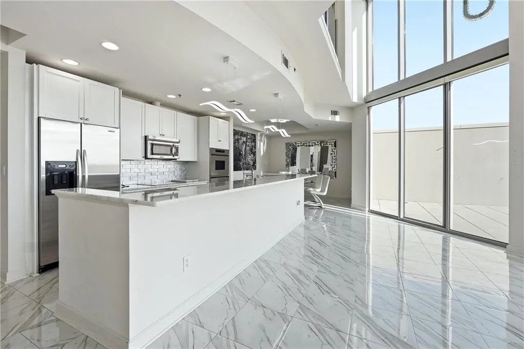 Kitchen with light marble finish floors, white cabinets, stainless steel appliances, a kitchen island with sink, and light stone counters