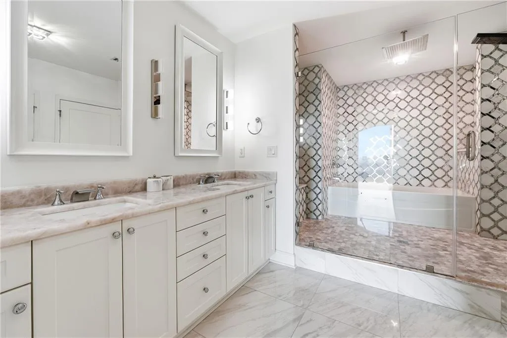 Full bath featuring double vanity, a stall shower, and light marble finish flooring