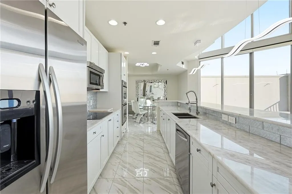 Kitchen featuring stainless steel appliances, light stone counters, white cabinets, light marble finish floors, and recessed lighting