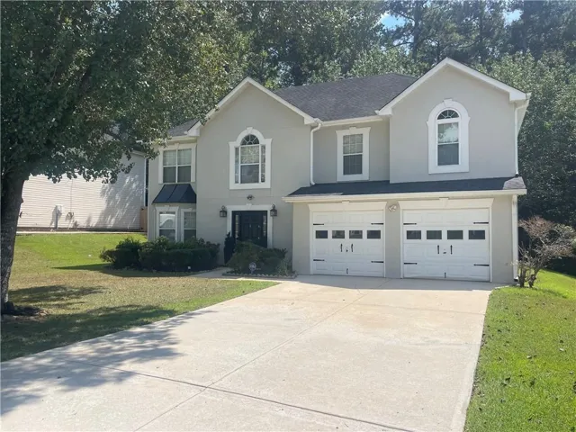Two-story stucco exterior featuring a two-car garage, manicured front lawn, and mature trees
