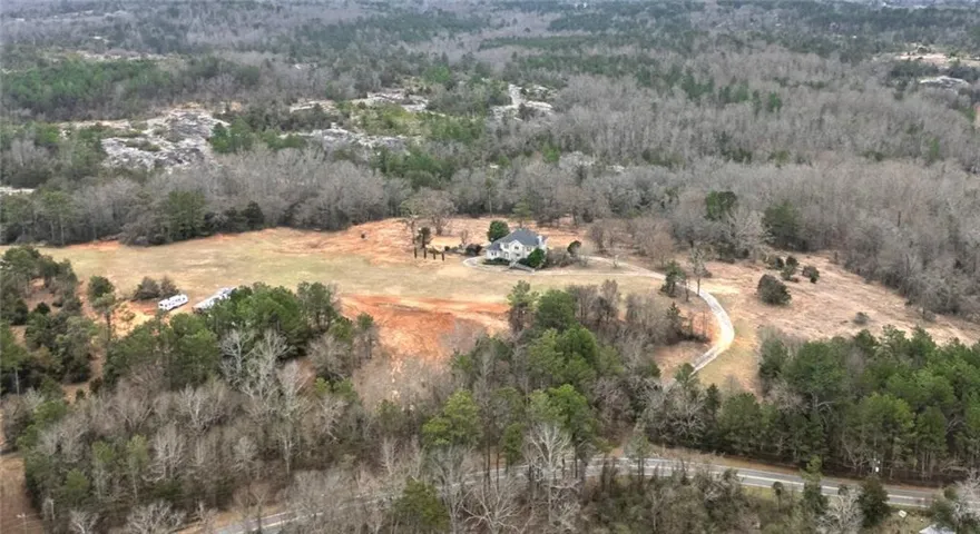 Expansive property featuring a residence, natural tree coverage, open fields, and a winding driveway