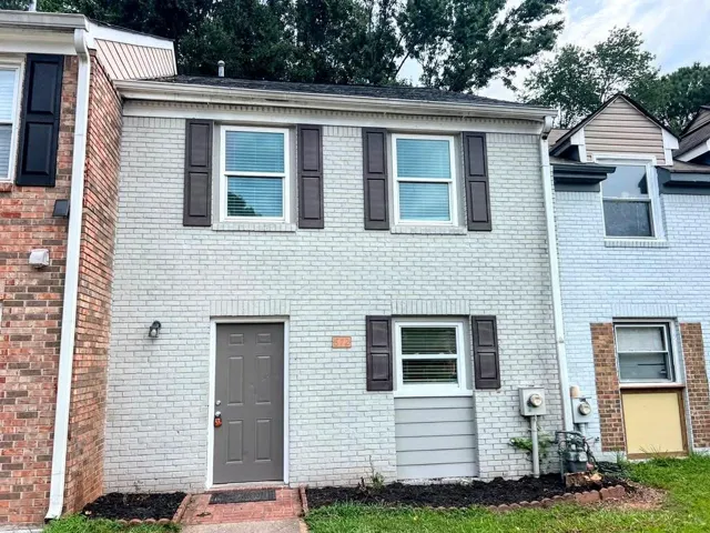 Two-story brick exterior with painted finish, featuring dark louvered shutters, a dark paneled entry door, and a manicured landscape bed
