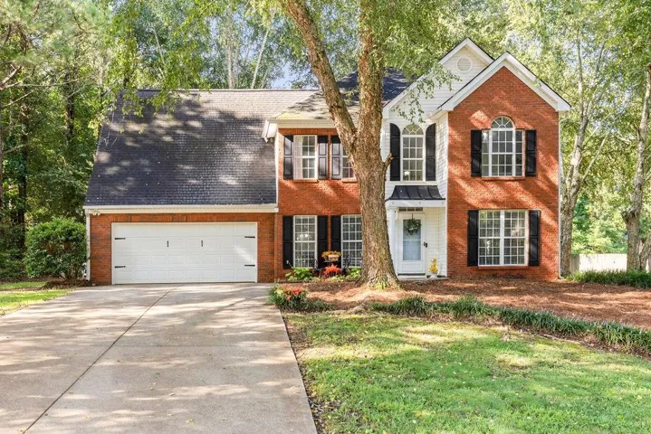 Two-story residence featuring a brick and siding exterior, arched window, attached two-car garage, and established landscaping