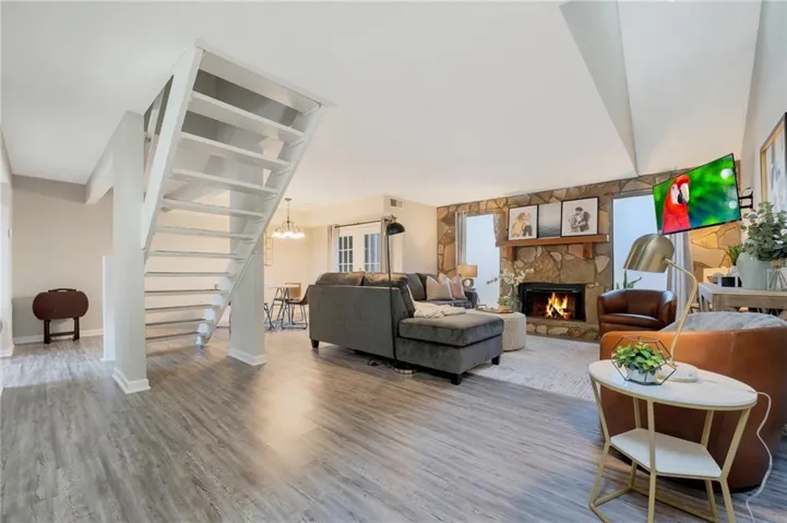 Living area with a stone fireplace, wood finished floors, stairs, and a chandelier