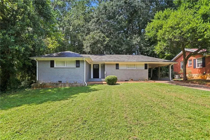 Ranch-style residence featuring a gray exterior, black shutters, a covered carport, and a front lawn with mature trees