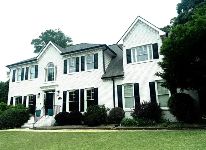 White brick exterior with black shutters, gabled rooflines, arched window, and landscaped shrubbery